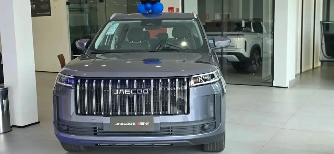 SUV Jaecoo 5 cinza exposto de frente no showroom de uma concessionária, com o logotipo da marca na grade dianteira