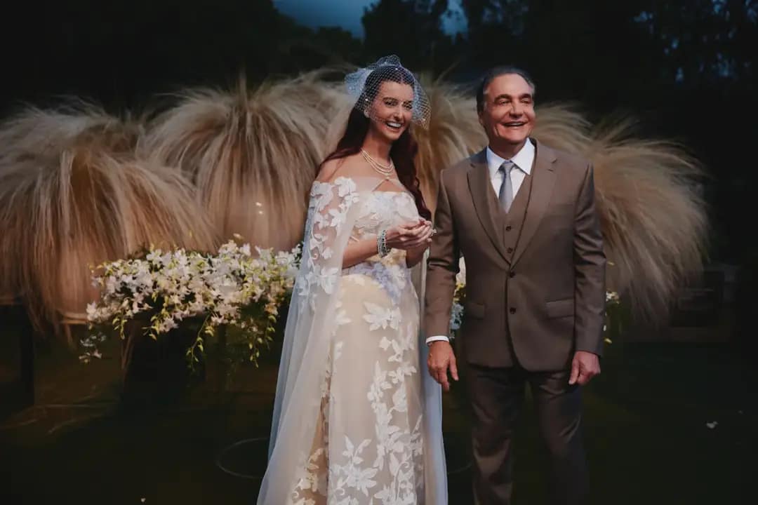 Duda Recoder, com vestido de noiva branco rendado e véu, ao lado de Euler Nejm, que veste terno marrom, durante o casamento