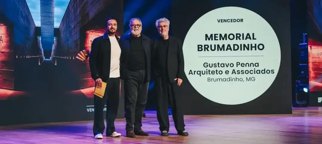 Gustavo Penna e outros dois homens posam ao lado do painel que anuncia o Memorial Brumadinho como vencedor do 3º Prêmio Projeto de Arquitetura