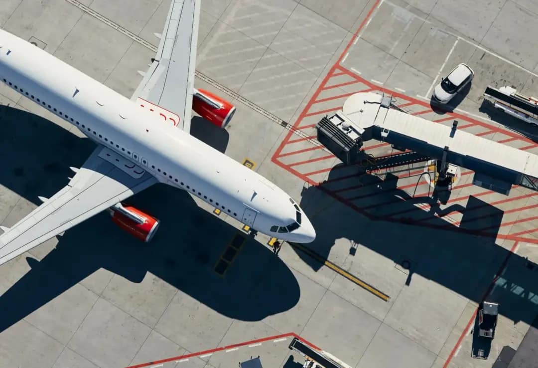 Avião comercial estacionado no pátio de um aeroporto, conectado a uma ponte de embarque, representa os destinos com passagens mais barata em novembro