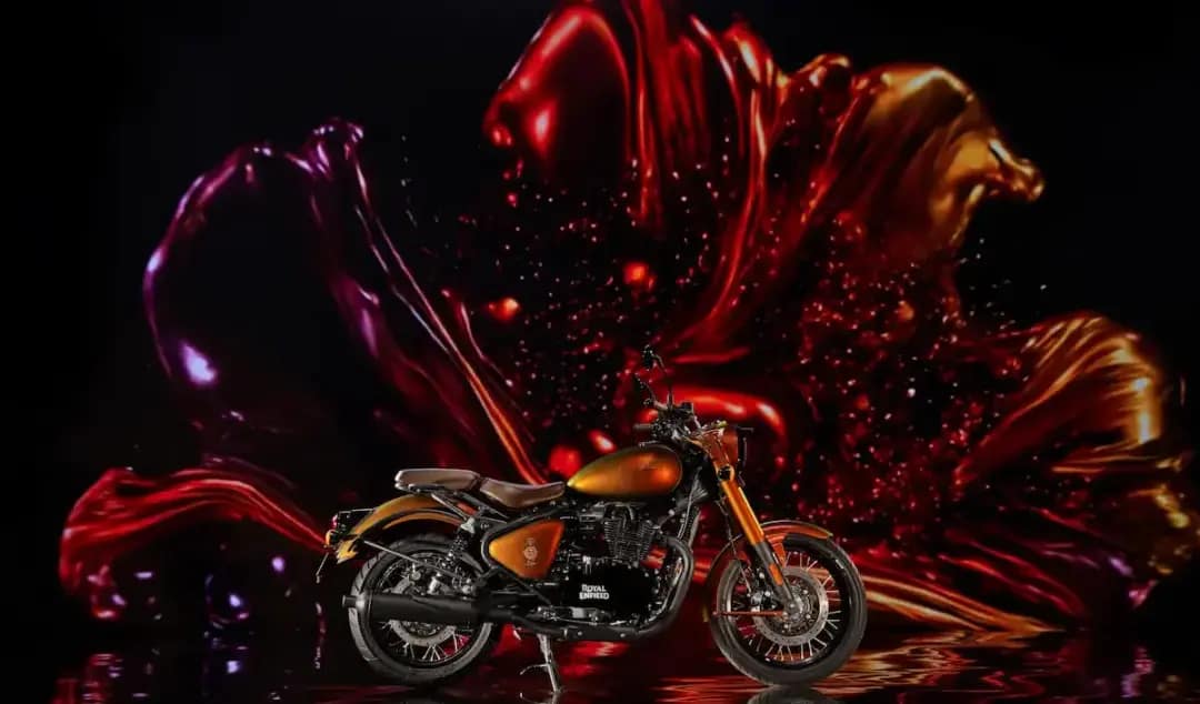 Motocicleta Royal Enfield Classic 650 Hypershift em tons de vermelho e dourado, com assento marrom e acabamento preto, exibida diante de um painel artístico iluminado