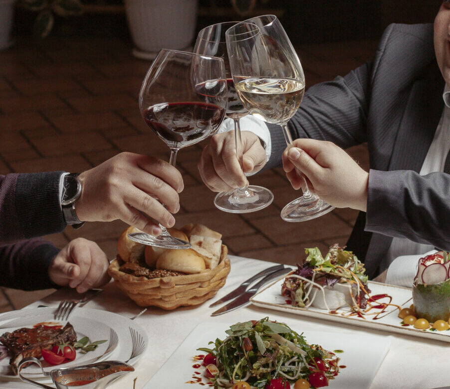 Three friends cheer wine glasses with red and white wine at dinn