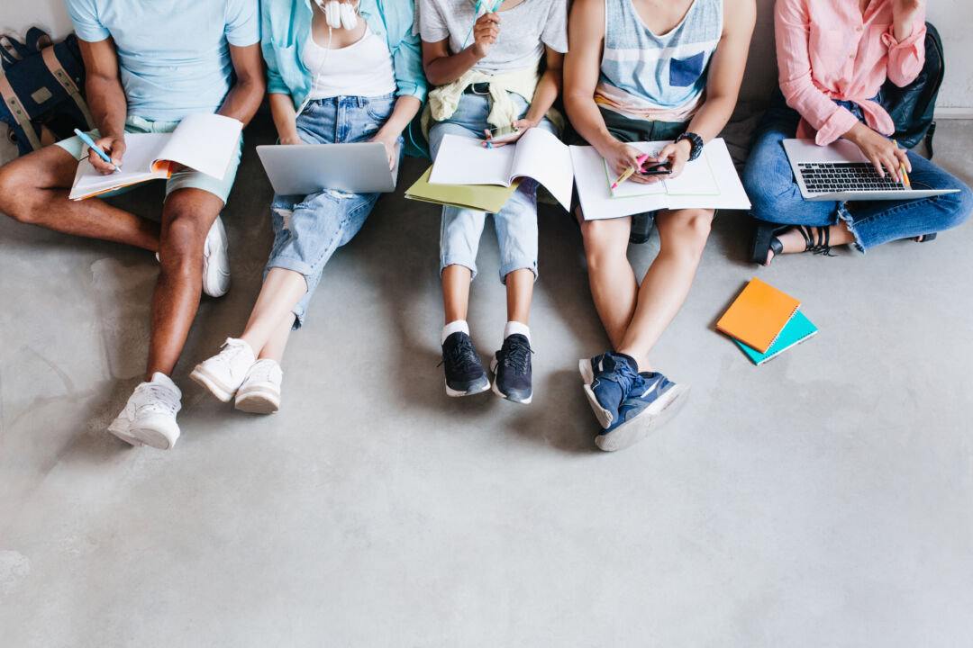 Overhead portrait of young people with laptops and smartphones, sitting together on the floor Students writing lectures holding textbooks on their knees