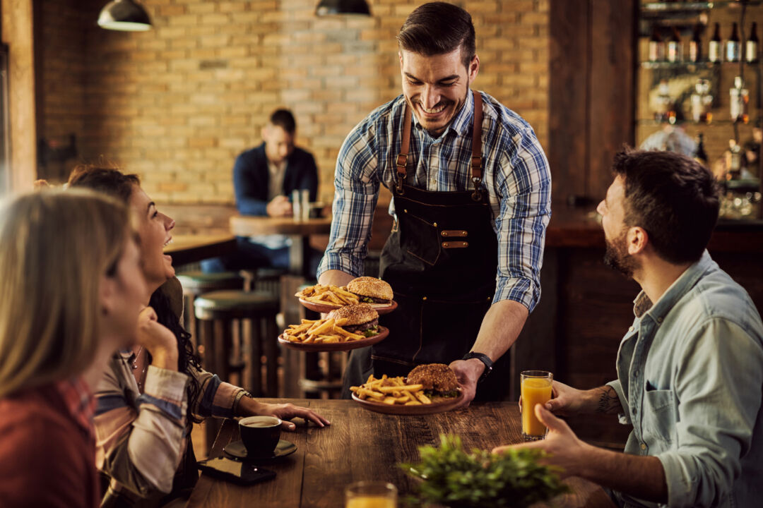 Happy waiter serving food to group of cheerful friends in a pub