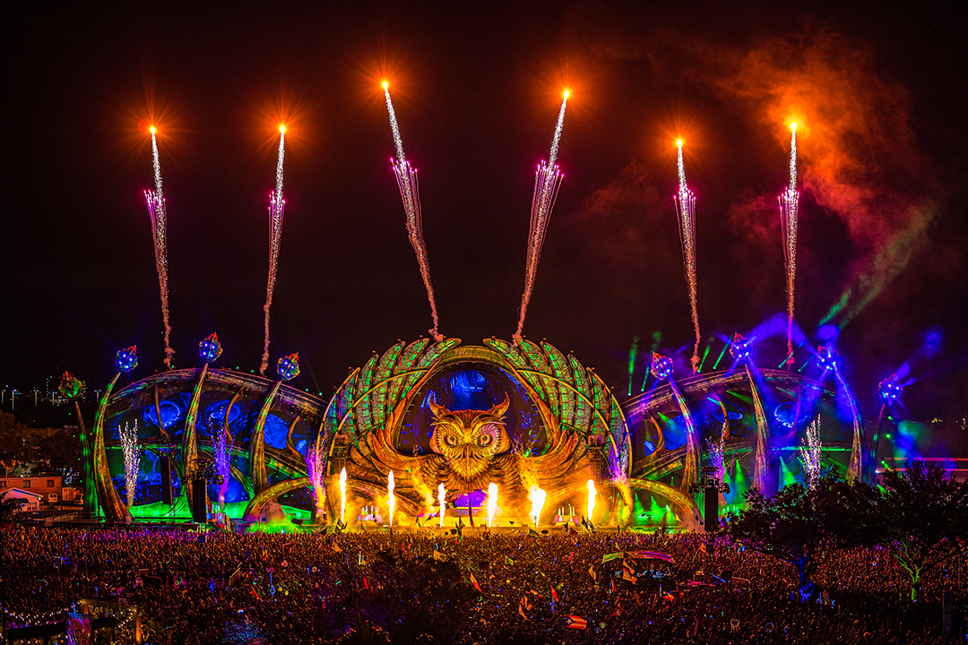 Fogos de artifício iluminam o palco principal do festival EDC durante show noturno, com estrutura em forma de coruja e milhares de pessoas na plateia