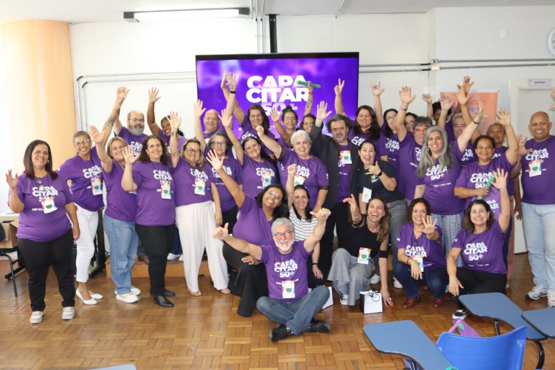 Grupo de alunos acima dos 50 anos posa sorridente com camisetas roxas durante a formatura do programa Capacitar 50+, promovido pelo Instituto Marina e Flávio Guimarães e pela Mais Vívida em Belo Horizonte.