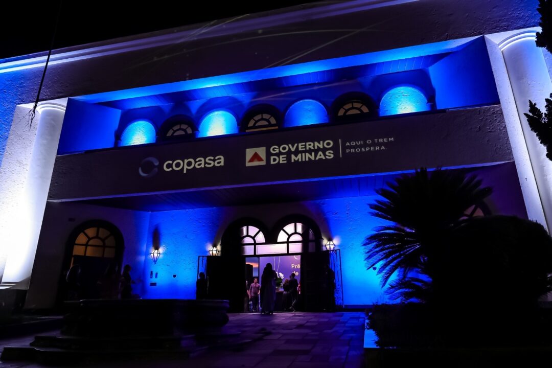 Fachada iluminada em azul durante o Prêmio Copasa de Jornalismo, em Belo Horizonte, com projeção dos logos da Copasa e do Governo de Minas
