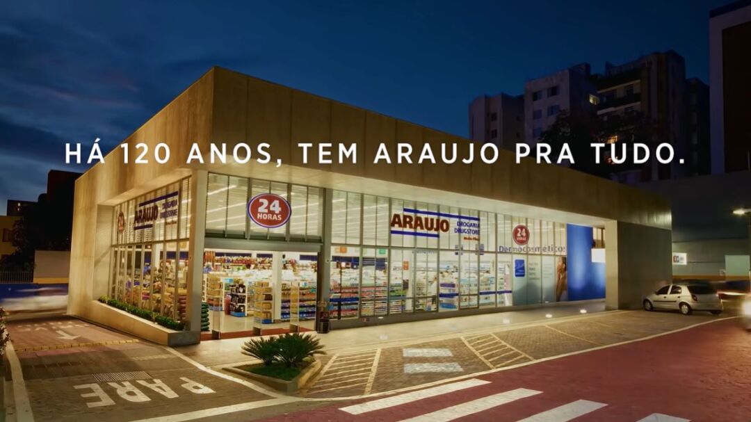 Fachada iluminada de unidade da Drogaria Araujo com campanha de 120 anos exibida na imagem