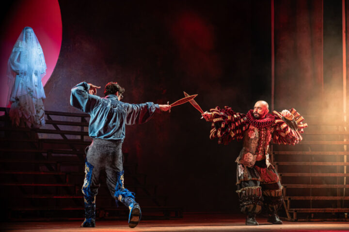 CCBB BH promove programação inspirada em “Romeu e Julieta de Parintins” Dois artistas se apresentam em palco iluminado com figurinos inspirados no Festival de Parintins durante cena teatral de “Romeu e Julieta de Parintins – Ecos da Selva”