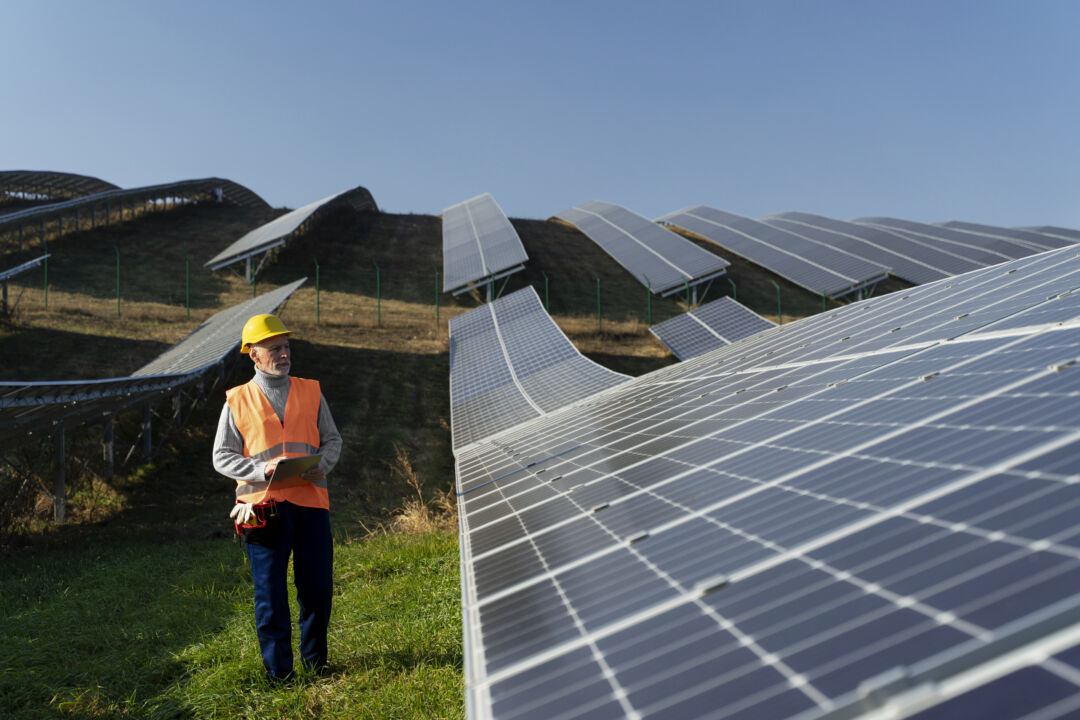 Usina de energia solar com painéis fotovoltaicos em operação e técnico realizando inspeção em campo aberto
