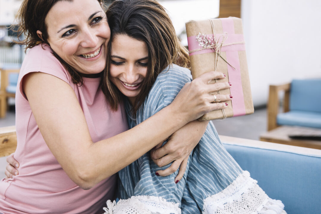 Filha abraça mãe enquanto entrega presente no Dia das Mães em momento de afeto