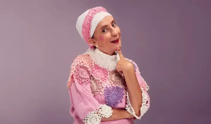 Gorete Milagres caracterizada como Filó, usando figurino de crochê rosa e branco - Quarteirão das Artes