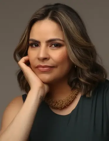A soprano Deborah Bulgarelli posa para retrato com blusa preta, colar dourado e cabelos castanhos com mechas claras