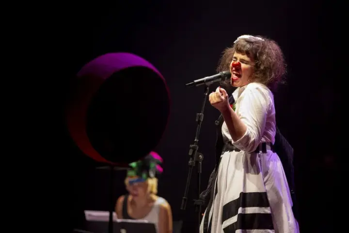 Tom Menor com Mariana Arruda no Festival Sesi em Cena Palhaça Begônia, interpretada por Mariana Arruda, canta ao microfone durante o espetáculo infantil Tom Menor, que apresenta clássicos de Tom Jobim com humor e música no Festival Sesi em Cena