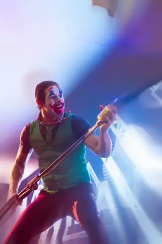 Artista caracterizado como palhaço se apresenta com microfone em palco iluminado durante espetáculo musical, em imagem relacionada à programação de Halloween do Underground Black Pub, em Belo Horizonte