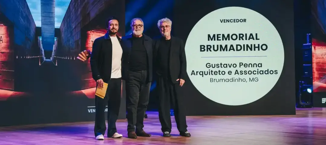 Gustavo Penna e outros dois homens posam ao lado do painel que anuncia o Memorial Brumadinho como vencedor do 3º Prêmio Projeto de Arquitetura